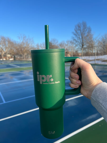 Person holding the IPR cup with a tennis court in the background